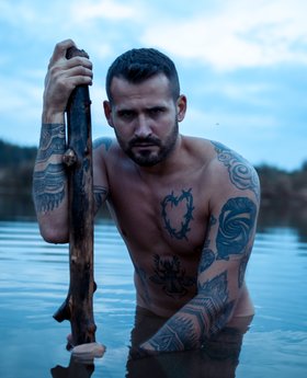 Naked man tattooed all over his body poses in the lake