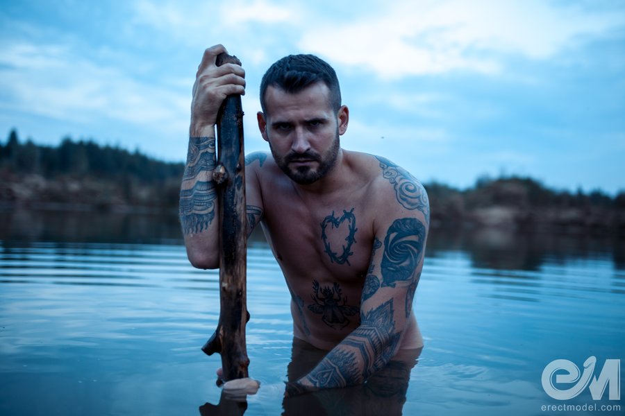 Naked man tattooed all over his body poses in the lake